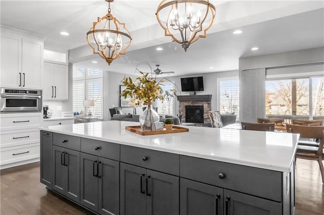 kitchen featuring dark wood-style floors, gray cabinetry, light countertops, a stone fireplace, and stainless steel oven