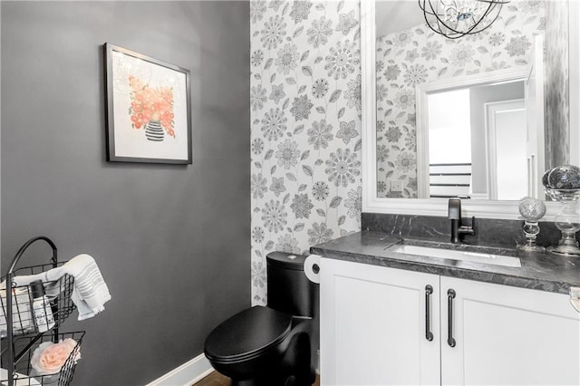 bathroom with toilet, wallpapered walls, baseboards, and vanity