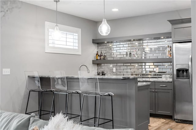 kitchen featuring light wood finished floors, a kitchen breakfast bar, light stone countertops, gray cabinets, and stainless steel refrigerator with ice dispenser