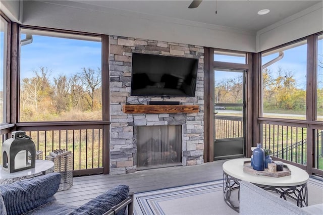 sunroom / solarium with ceiling fan, a wealth of natural light, and a stone fireplace