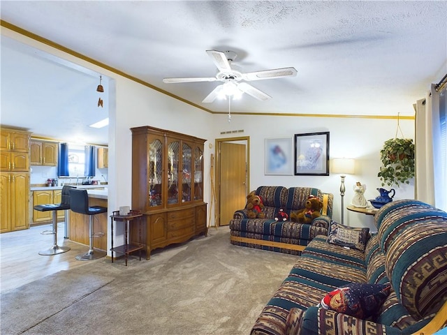 living room with ceiling fan, a textured ceiling, light colored carpet, vaulted ceiling, and crown molding