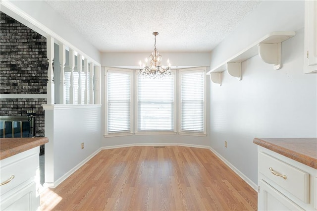 unfurnished dining area with light wood-type flooring, a brick fireplace, a textured ceiling, and a notable chandelier