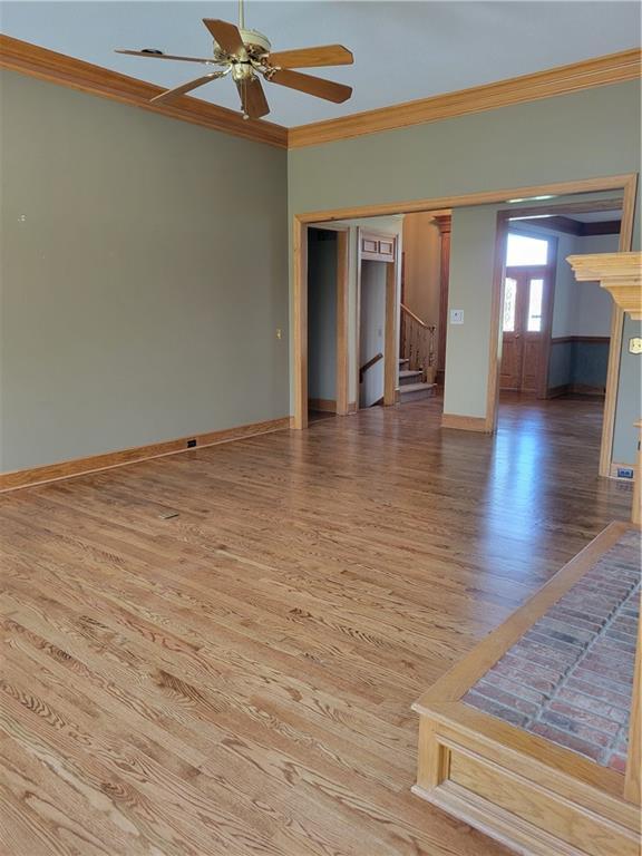 empty room featuring wood finished floors, ornamental molding, stairway, ceiling fan, and baseboards