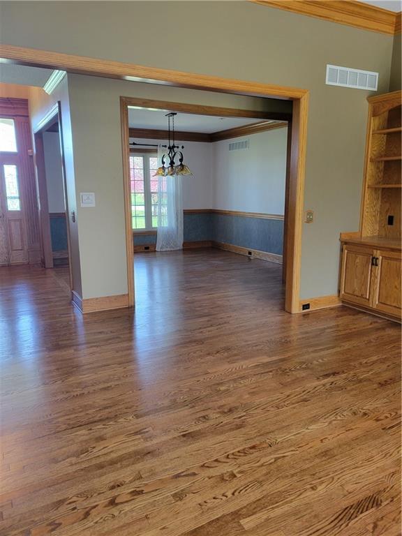 unfurnished dining area featuring a chandelier, ornamental molding, visible vents, and wood finished floors