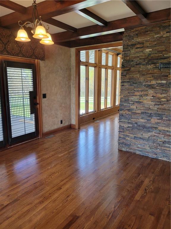 unfurnished room featuring a notable chandelier, beam ceiling, plenty of natural light, and dark wood-type flooring