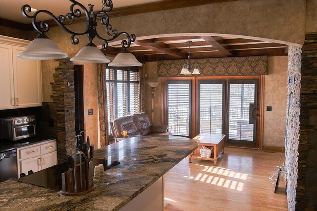 dining room featuring a toaster, coffered ceiling, light wood finished floors, arched walkways, and beam ceiling
