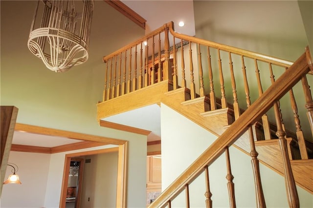 staircase featuring recessed lighting, an inviting chandelier, crown molding, and a high ceiling
