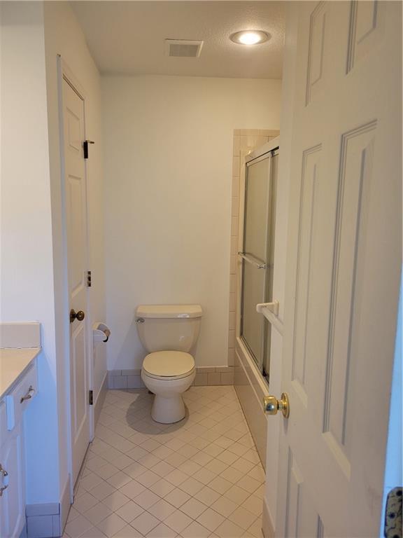 bathroom featuring toilet, combined bath / shower with glass door, visible vents, tile patterned flooring, and vanity