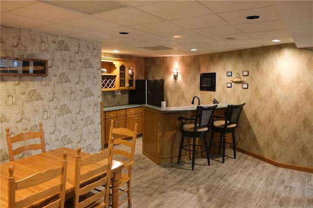 bar featuring light wood finished floors, black fridge, a paneled ceiling, baseboards, and wet bar