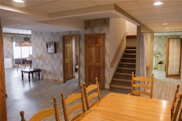 dining space with stairs, wood finished floors, a paneled ceiling, baseboards, and wallpapered walls