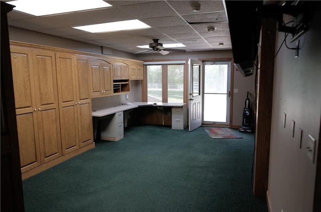 unfurnished office featuring carpet, built in study area, a drop ceiling, and a ceiling fan