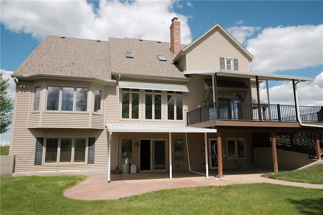 rear view of property featuring a chimney, a lawn, a deck, a shingled roof, and a patio area