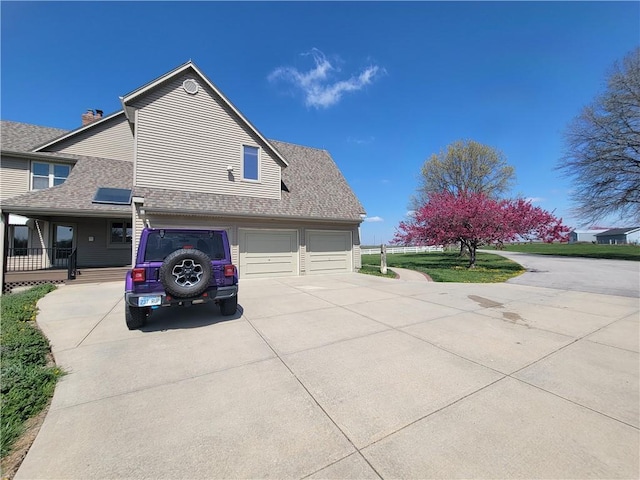 view of side of property with an attached garage, a shingled roof, and driveway