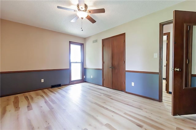 interior space with light wood-type flooring, ceiling fan, a closet, and a textured ceiling