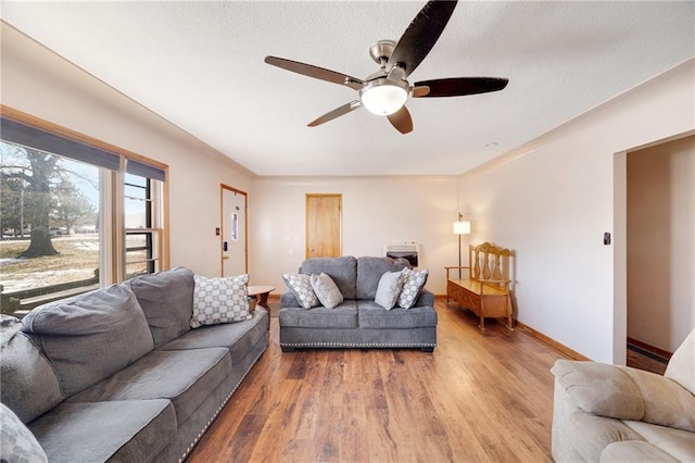 living room featuring ceiling fan, a textured ceiling, light wood-type flooring, and baseboards