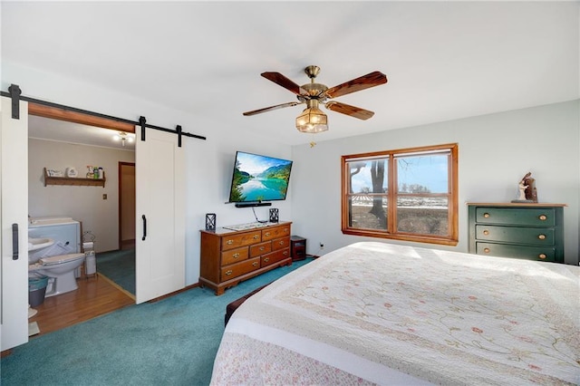 bedroom with a barn door, ensuite bathroom, carpet floors, and ceiling fan