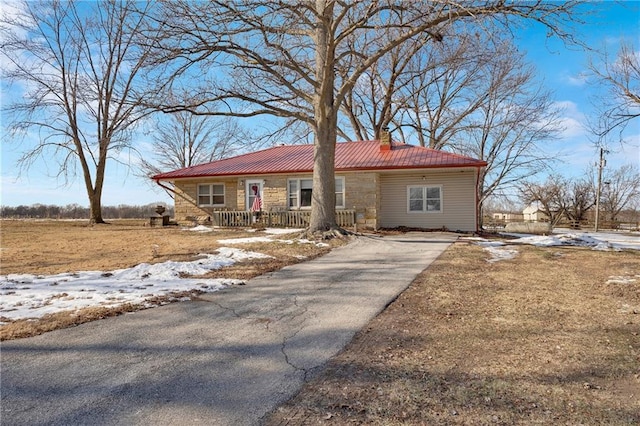 view of front of property with driveway, stone siding, covered porch, metal roof, and a chimney