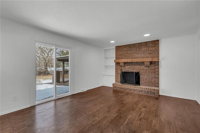 unfurnished living room featuring a brick fireplace, dark wood-type flooring, and built in shelves