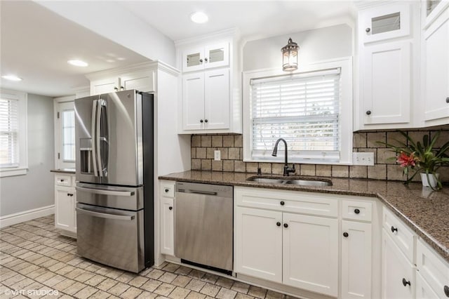 kitchen featuring a sink, white cabinetry, appliances with stainless steel finishes, dark stone countertops, and glass insert cabinets