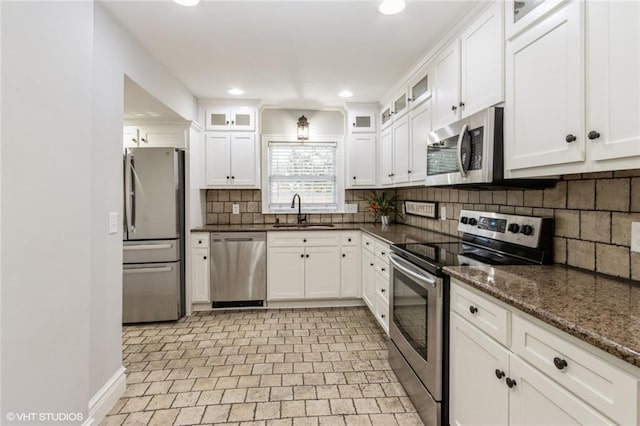 kitchen with a sink, white cabinetry, appliances with stainless steel finishes, dark stone countertops, and glass insert cabinets