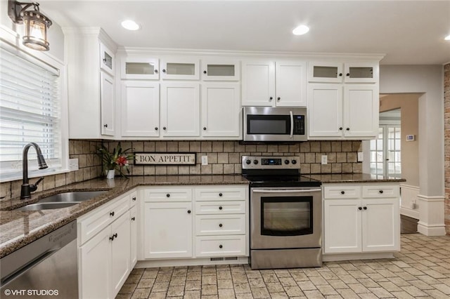 kitchen with appliances with stainless steel finishes, dark stone countertops, a sink, and white cabinetry