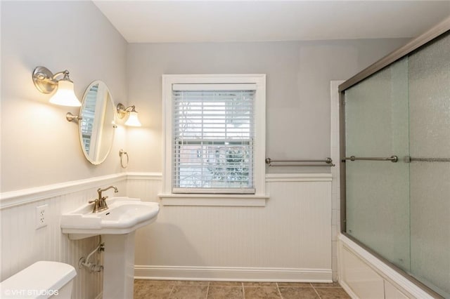 full bathroom with tile patterned flooring, wainscoting, toilet, and combined bath / shower with glass door