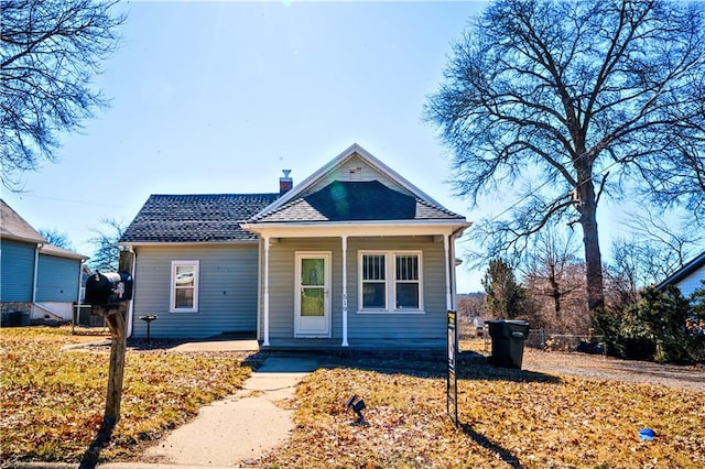 bungalow with a porch, a shingled roof, a chimney, and central air condition unit