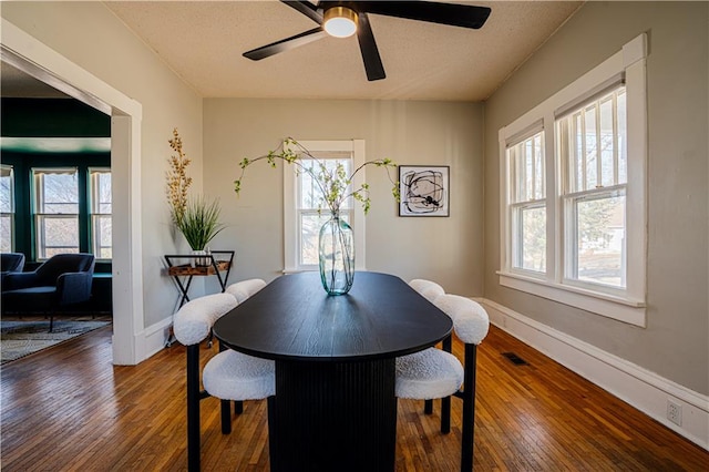 dining area featuring baseboards, visible vents, ceiling fan, and dark wood-type flooring