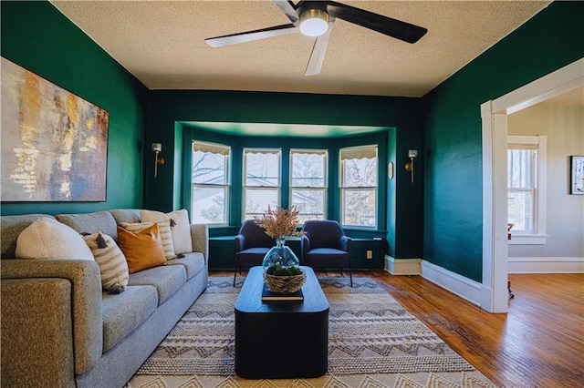 living room featuring ceiling fan, a textured ceiling, baseboards, and wood finished floors