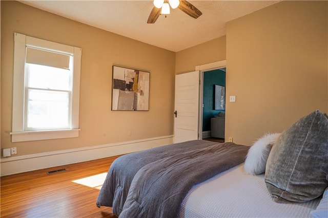 bedroom featuring a ceiling fan, wood finished floors, visible vents, and baseboards