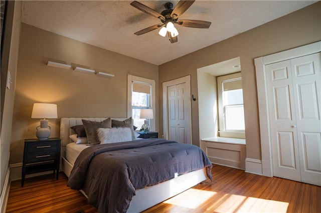 bedroom featuring a textured ceiling, multiple windows, two closets, and wood finished floors