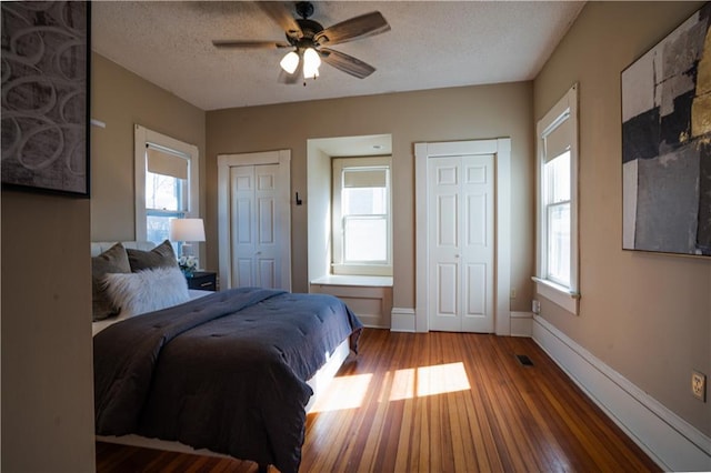 bedroom with wood finished floors, multiple windows, a textured ceiling, and two closets