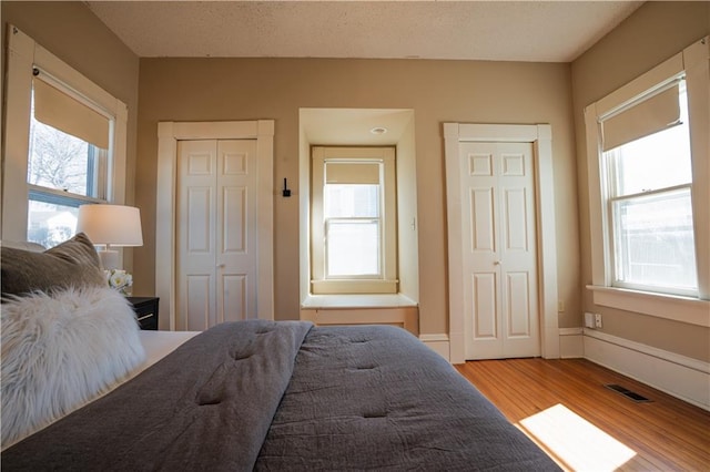 bedroom with light wood-style flooring, multiple closets, visible vents, and baseboards