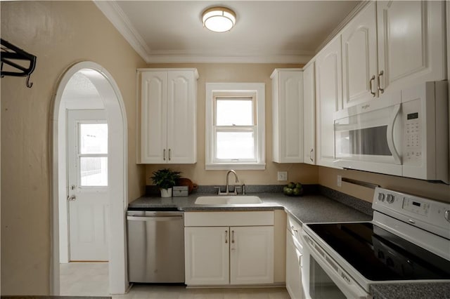 kitchen with dark countertops, white appliances, white cabinetry, and a sink