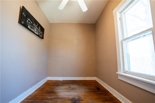 empty room with dark wood-style floors, a ceiling fan, visible vents, and baseboards