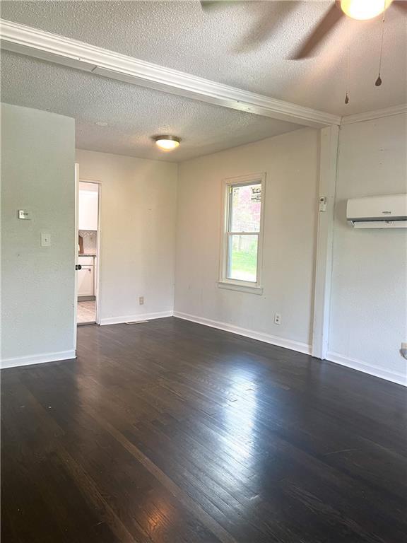 empty room with dark wood-type flooring, a textured ceiling, and a wall mounted air conditioner