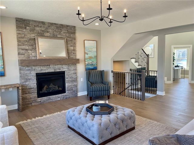 living room with a stone fireplace, a chandelier, and light hardwood / wood-style flooring