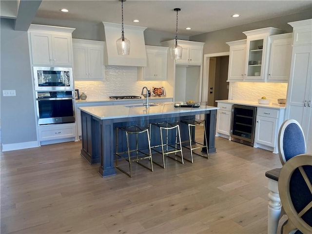 kitchen featuring appliances with stainless steel finishes, decorative light fixtures, white cabinetry, wine cooler, and a kitchen island with sink