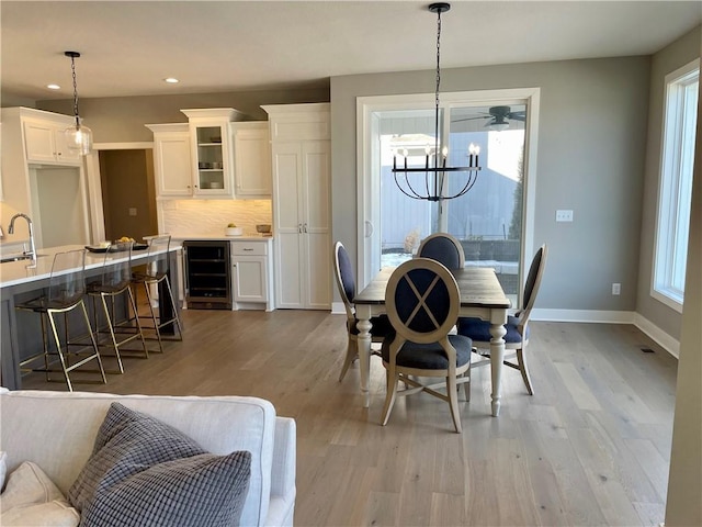 dining room featuring an inviting chandelier, light hardwood / wood-style floors, beverage cooler, and a healthy amount of sunlight