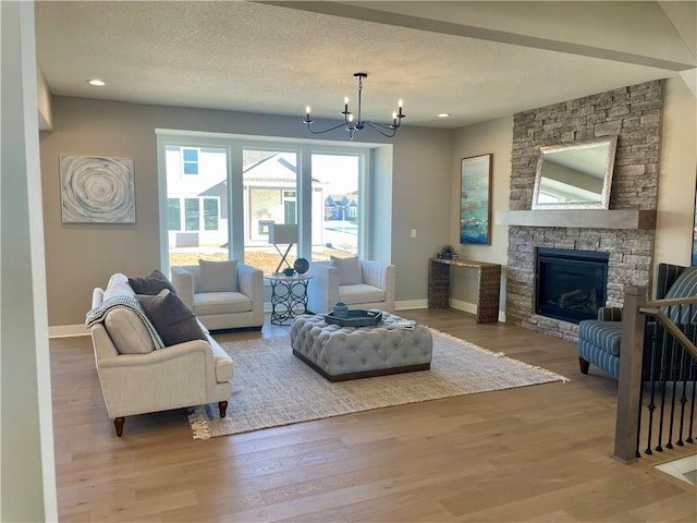 living room featuring an inviting chandelier, wood-type flooring, a stone fireplace, and a textured ceiling