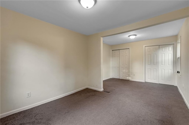 unfurnished bedroom with two closets and dark carpet