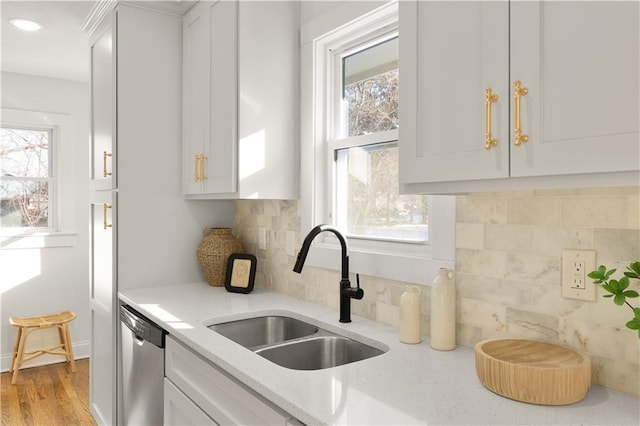 kitchen with stainless steel dishwasher, decorative backsplash, sink, white cabinets, and light stone counters