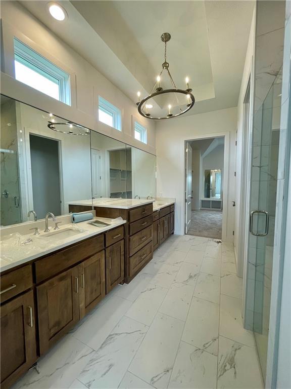 18300 Monrovia St, Overland Park, KS 66013 - bathroom featuring a shower stall, vanity, a tray ceiling, a chandelier, and marble finish flooring