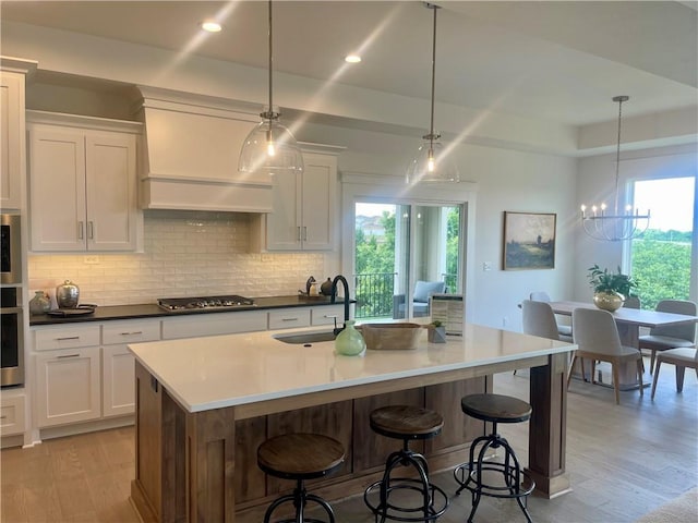 18300 Monrovia St, Overland Park, KS 66013 - kitchen featuring appliances with stainless steel finishes, light wood-type flooring, decorative backsplash, custom exhaust hood, and white cabinets