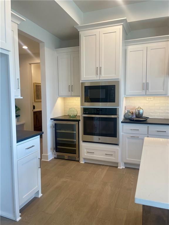 18300 Monrovia St, Overland Park, KS 66013 - kitchen featuring beverage cooler, stainless steel appliances, white cabinetry, and light wood-style flooring