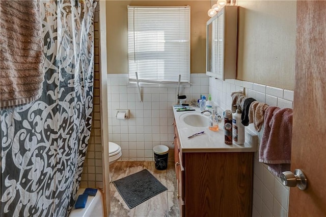 bathroom with toilet, vanity, and tile walls