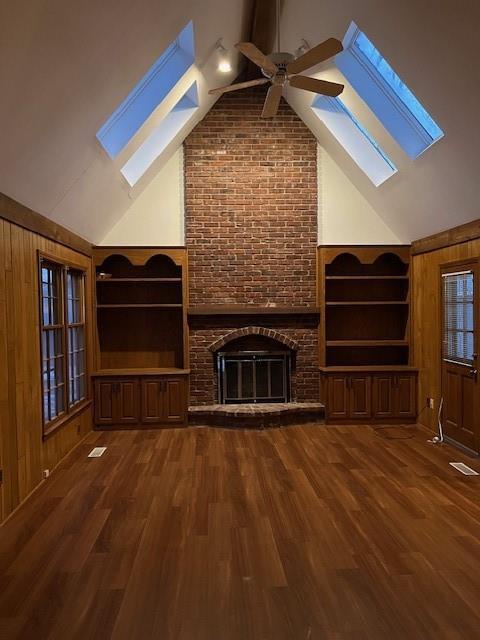 unfurnished living room featuring a brick fireplace, wooden walls, dark hardwood / wood-style floors, and ceiling fan