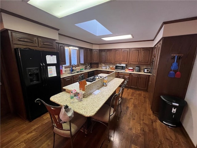 kitchen featuring stainless steel microwave, a sink, black fridge, crown molding, and a skylight