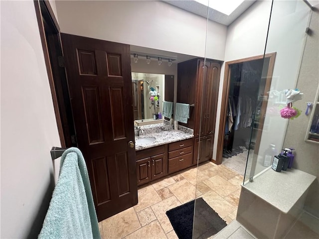bathroom featuring stone finish flooring, rail lighting, a walk in shower, vanity, and a skylight