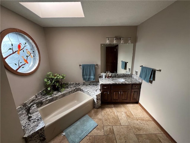 full bath with baseboards, a skylight, vanity, stone tile floors, and a garden tub